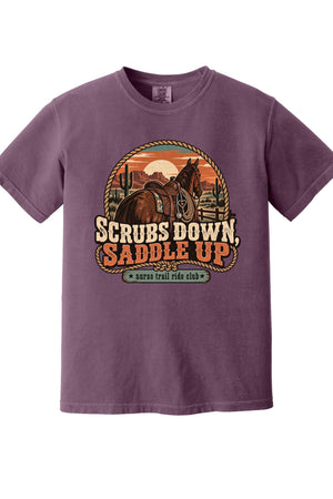 A purple short-sleeve crewneck t-shirt featuring a retro western-themed graphic of a horse rider on a trail with the text 'SCRUBS DOWN, SADDLE UP' and 'survival ride club'.