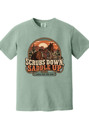 A sage green short-sleeve t-shirt with a retro western graphic of a horse and the text 'SCRUBS DOWN, SADDLE UP' and 'santa trail ride club'.