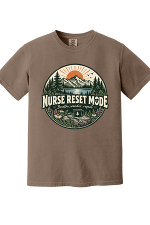 A brown short-sleeve crewneck t-shirt featuring a circular graphic on the chest with a mountain, pine trees, and the text 'NURSE RESET MODE'.
