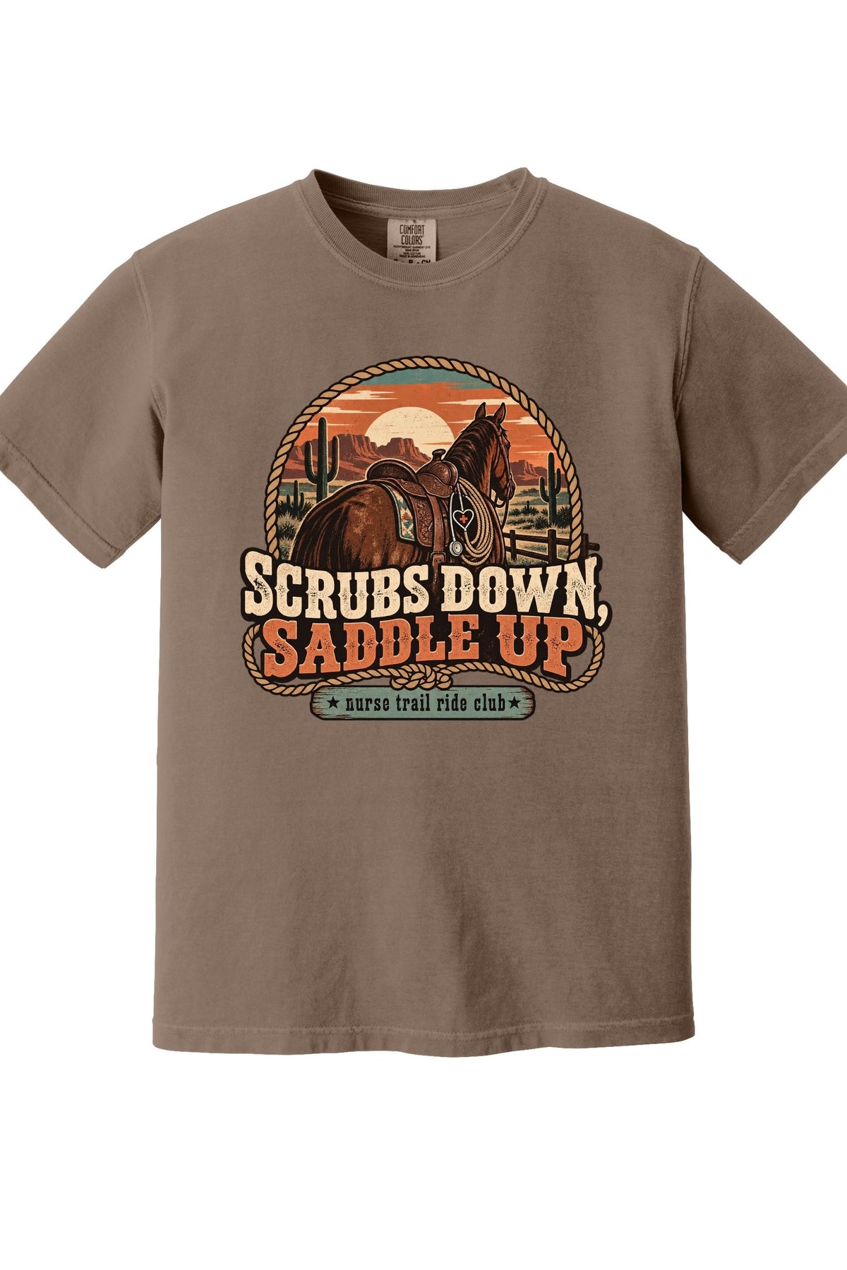 A brown short-sleeve crewneck t-shirt featuring a retro western graphic of a horse rider on a horse, with the text 'SCRUBS DOWN, SADDLE UP' and 'surf trail ride club' on a white background.