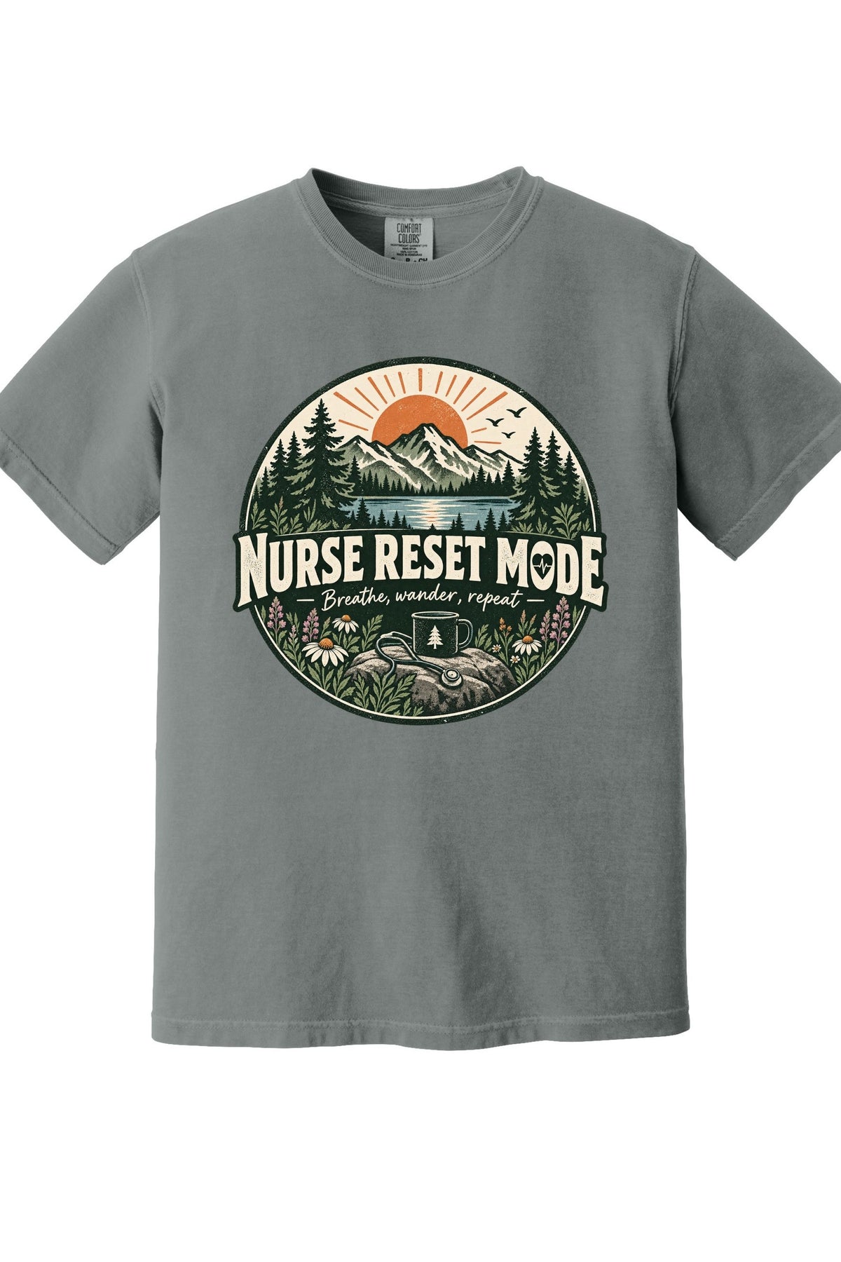 A heather gray short-sleeve crewneck t-shirt featuring a circular graphic on the chest with a mountain, pine trees, and a sunrise, with the text 'NURSE RESET MODE' and 'Breathe, wonder, repeat'.